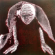 A woman crawls along the ground. She is bald, skeletal and covered in a removal blanket. Printed and tinted/shaded in black and red.
