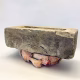 Soft sculpture head crushed by a brick