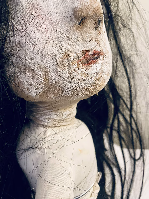 Uncanny girl doll with long dark brown hair. Face profile view close-up mouth.