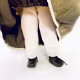 A doll wearing a sage green velvet and cream cotton dress. Uplifted skirt to show its legs.