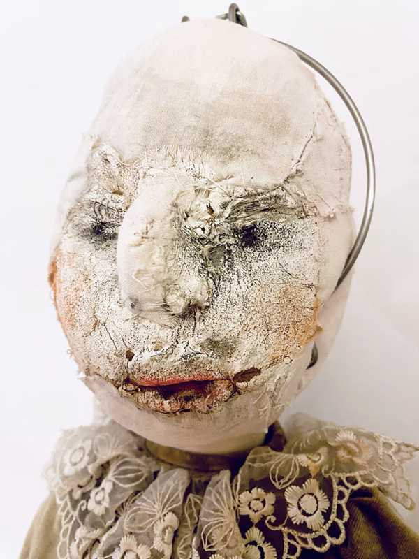 A doll wearing a sage green velvet and cream cotton dress. With a kilner jar clip over its head. Head view close-up.