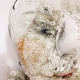 A doll wearing a sage green velvet and cream cotton dress. With a kilner jar clip over its head. Head view close-up.