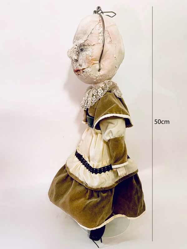A doll wearing a sage green velvet and cream cotton dress. With a kilner jar clip over its head.