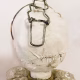 A doll wearing a sage green velvet and cream cotton dress. With a kilner jar clip over its head. Head view close-up.