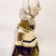 A doll wearing a sage green velvet and cream cotton dress. With a kilner jar clip over its head.