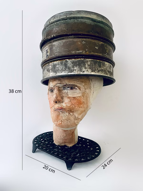 Head sculpture resting on a household iron trivet with a head piece of three stacked laboratory sieves.