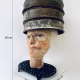 Head sculpture resting on a household iron trivet with a head piece of three stacked laboratory sieves.