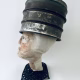 Head sculpture resting on a household iron trivet with a head piece of three stacked laboratory sieves.