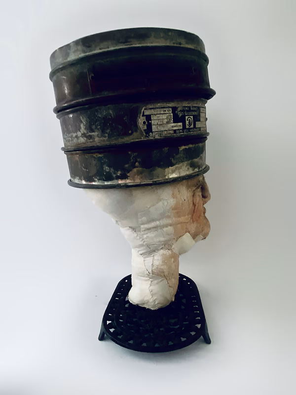 Head sculpture resting on a household iron trivet with a head piece of three stacked laboratory sieves.
