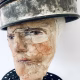 Close-up of head sculpture resting on a household iron trivet with a head piece of three stacked laboratory sieves.