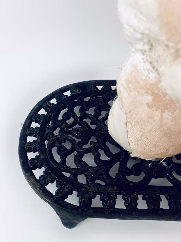 Base of head sculpture resting on a household iron trivet with a head piece of three stacked laboratory sieves.