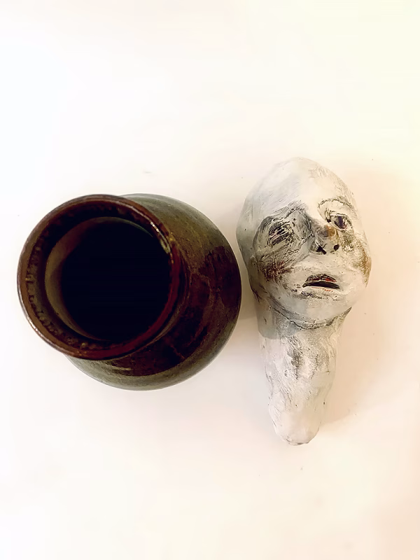 Small sculpture head next to ceramic pot