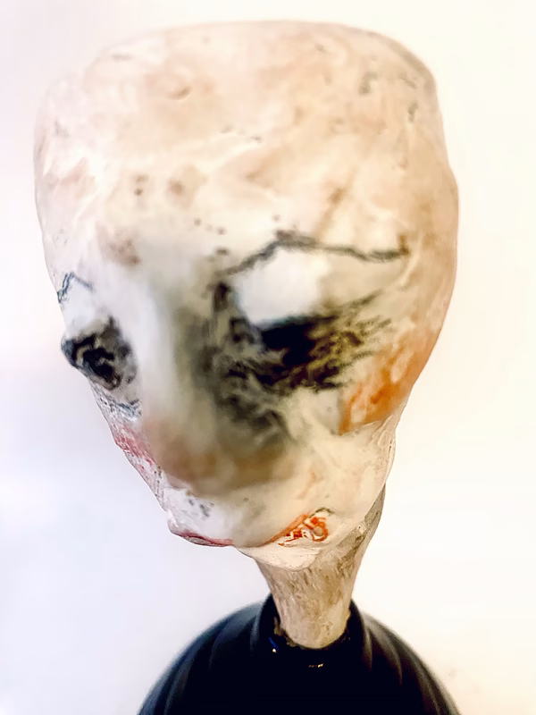 Small sculpture head emerging from ceramic pot (close-up)