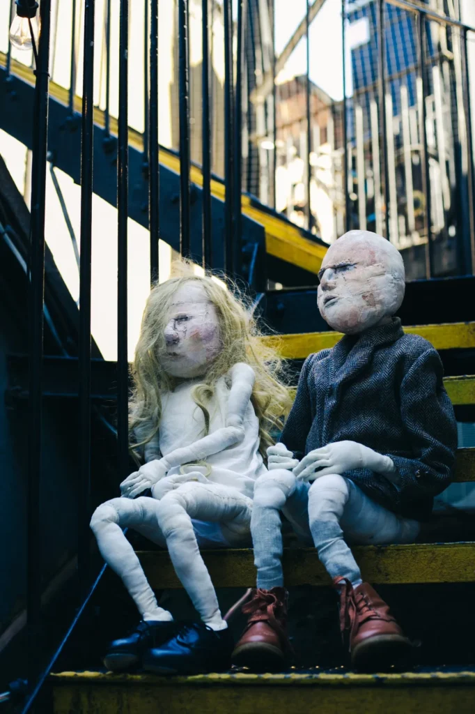 Two soft textile sculptures, a boy and a girl, sitting on an outer staircase